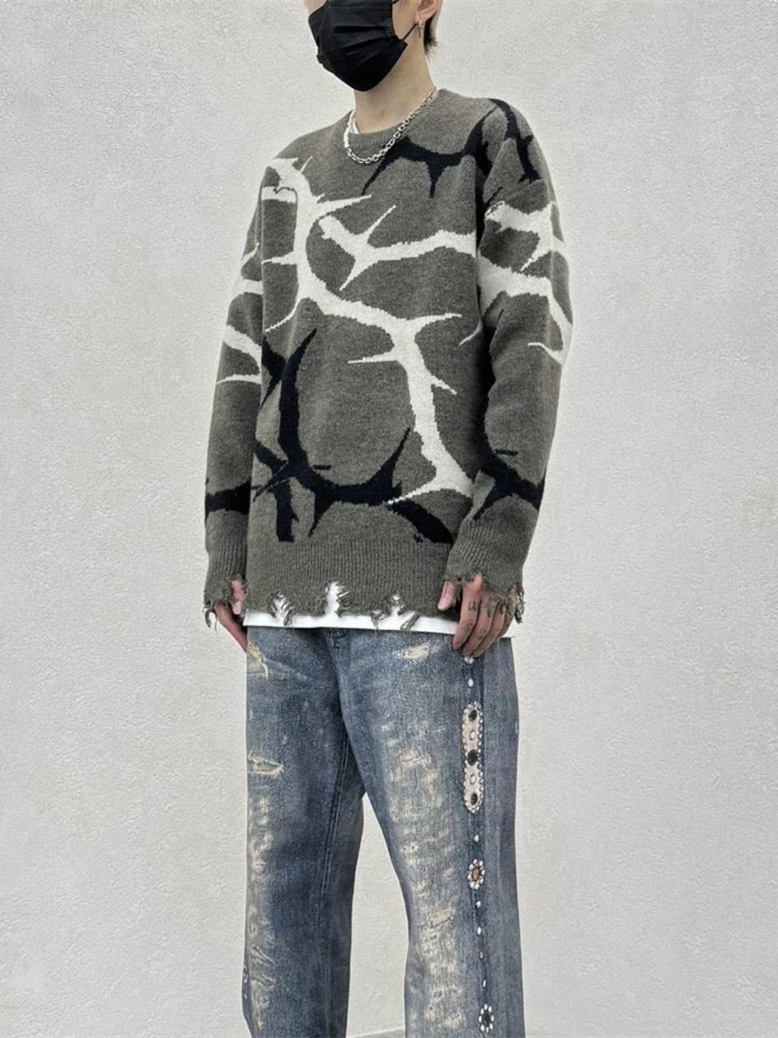 Model in a TALISHKO thorn-patterned sweater with distressed edges, wearing faded denim jeans.