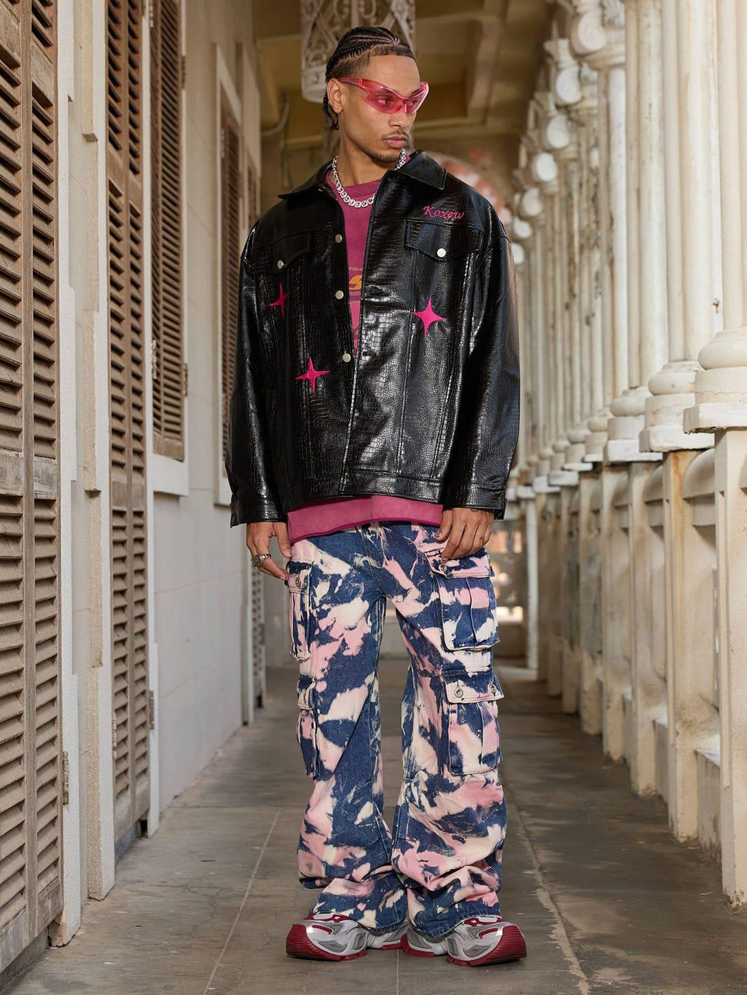 Model in TALISHKO tie-dye cargo jeans and black jacket, sporting pink sunglasses for a vibrant look.