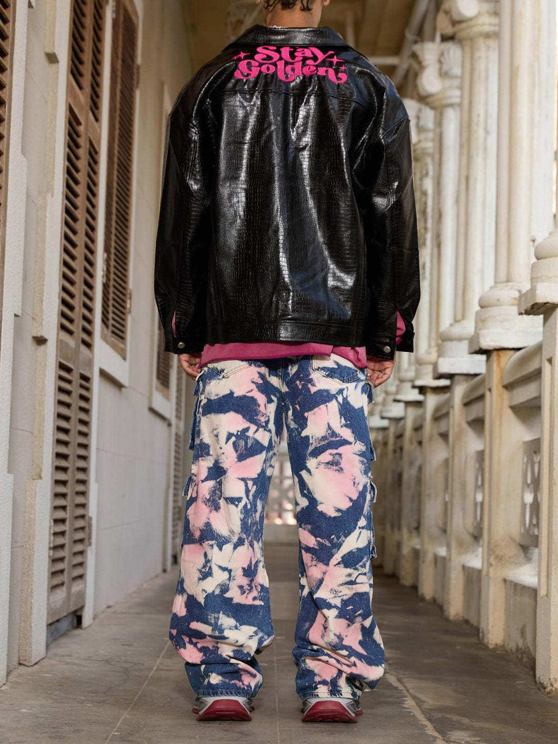 Model in TALISHKO tie-dye cargo jeans, back view, with glossy black jacket and pink lettering.