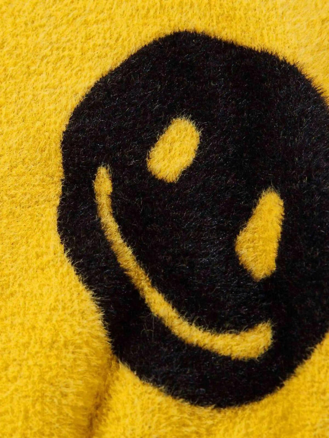 Zoomed-in texture of a yellow TALISHKO sweater featuring a bold black smiley face design.