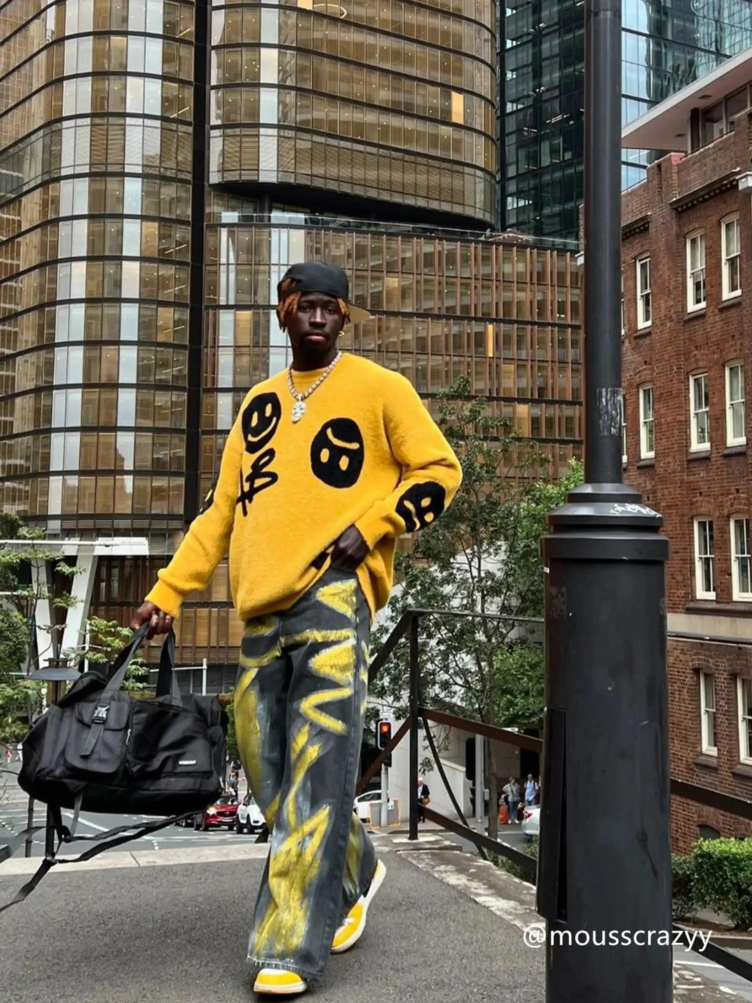 Model wearing a vibrant TALISHKO smiley face sweater, styled with artistic jeans in an urban setting.