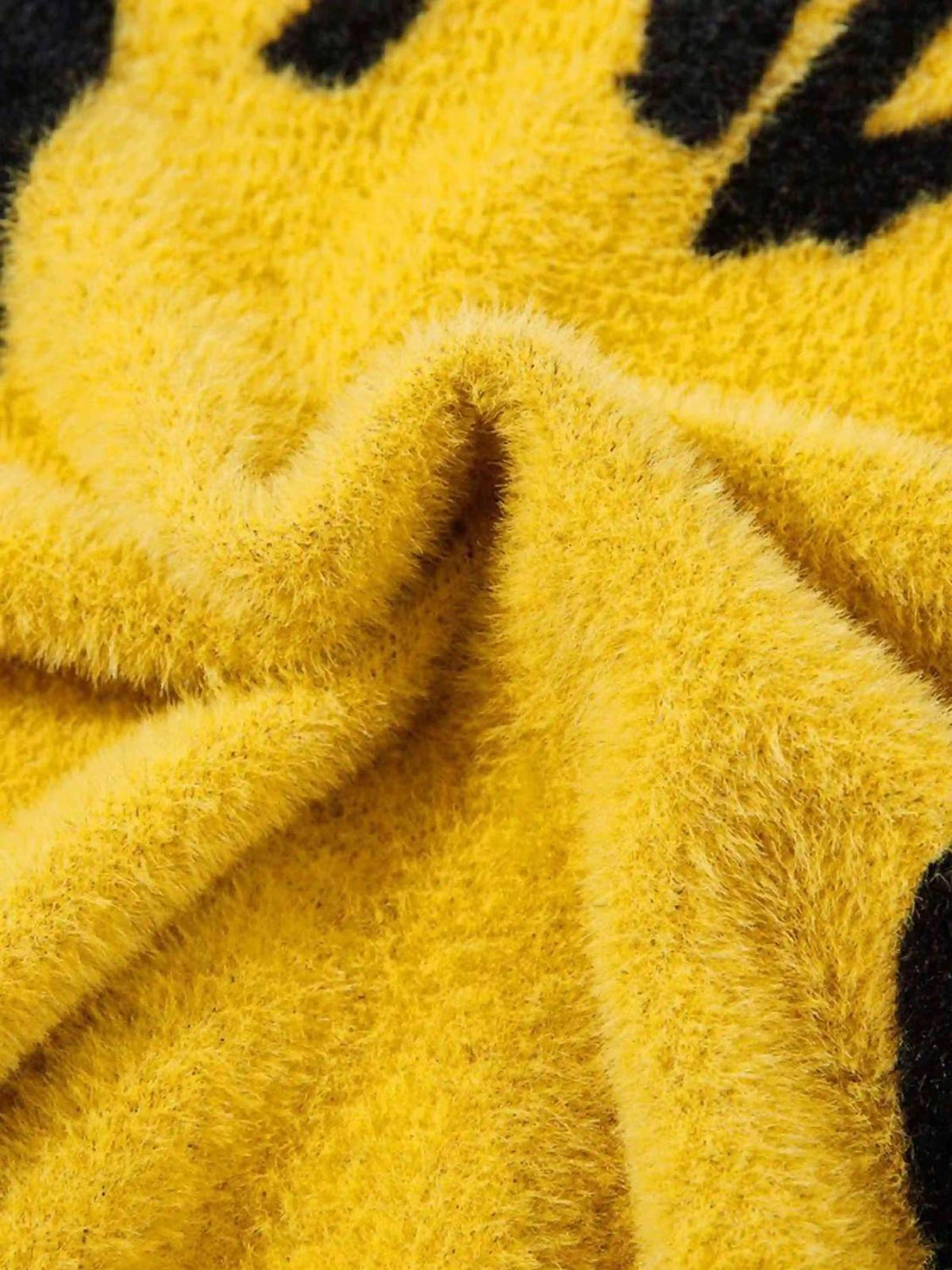 Detailed fabric and texture of a yellow TALISHKO sweater with contrasting black design elements.