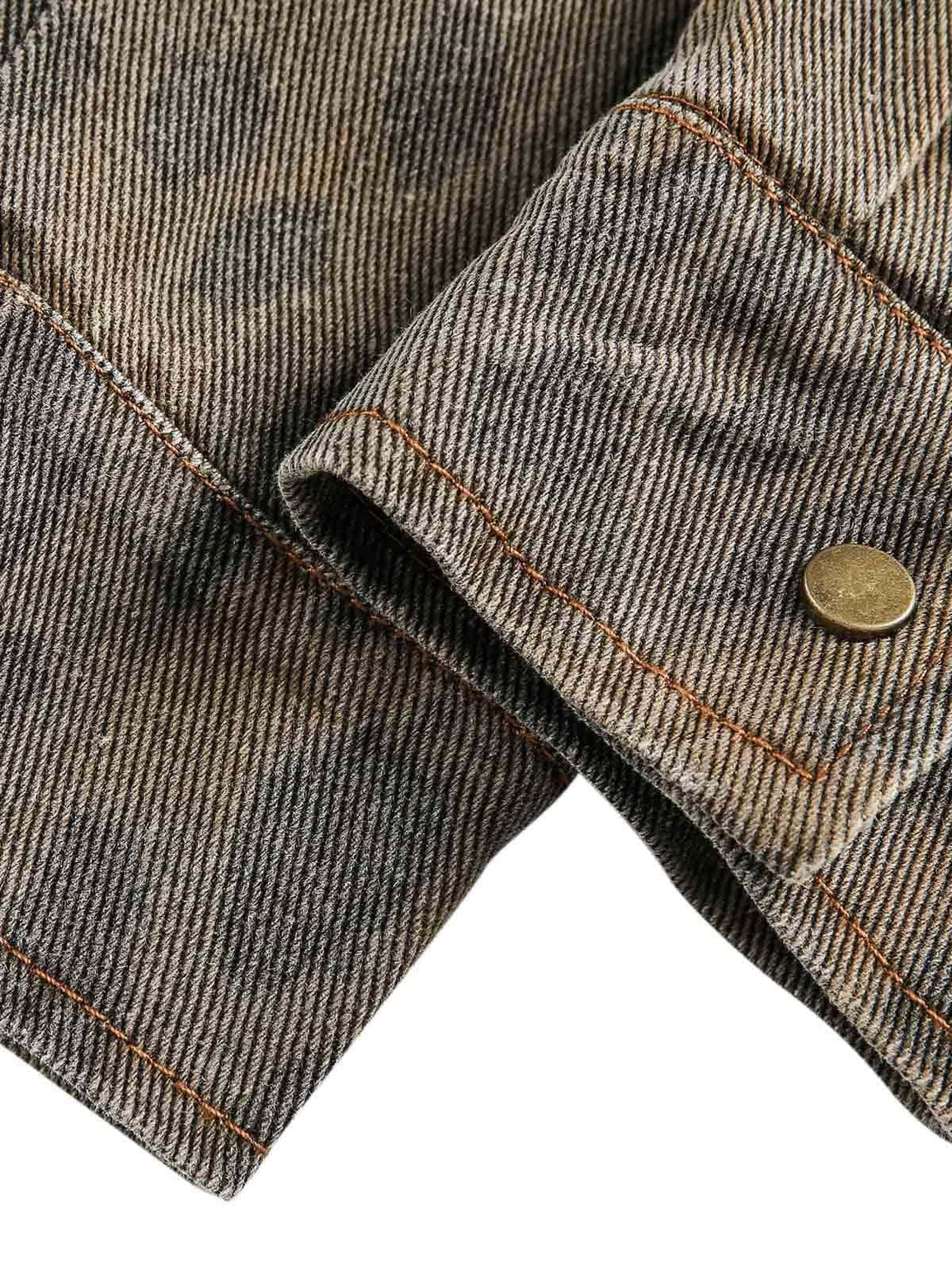A detailed view of TALISHKO's distressed cheetah print denim shirt cuff with brass button.