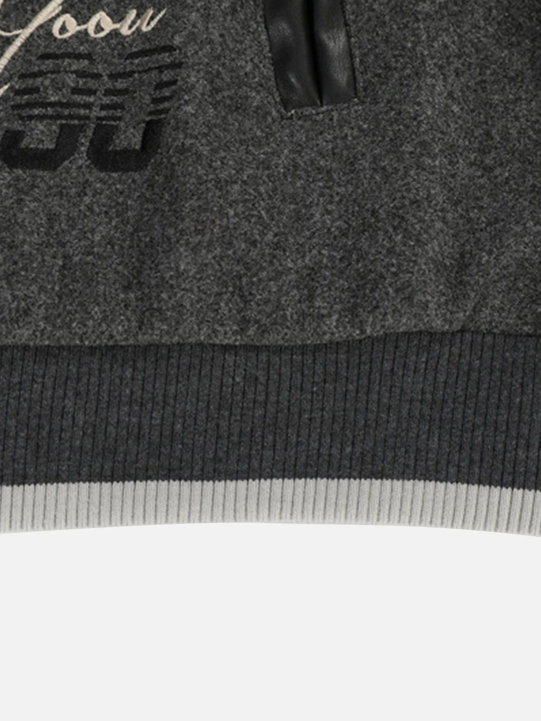 Zoomed-in texture of a gray varsity baseball jacket by TALISHKO with embroidered details.