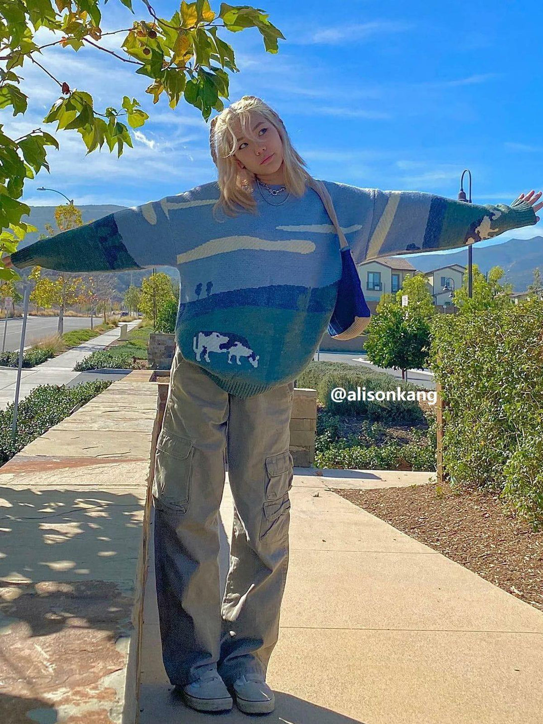 A model showcases a TALISHKO streetwear sweater with a playful cow pattern, paired with cargo pants.