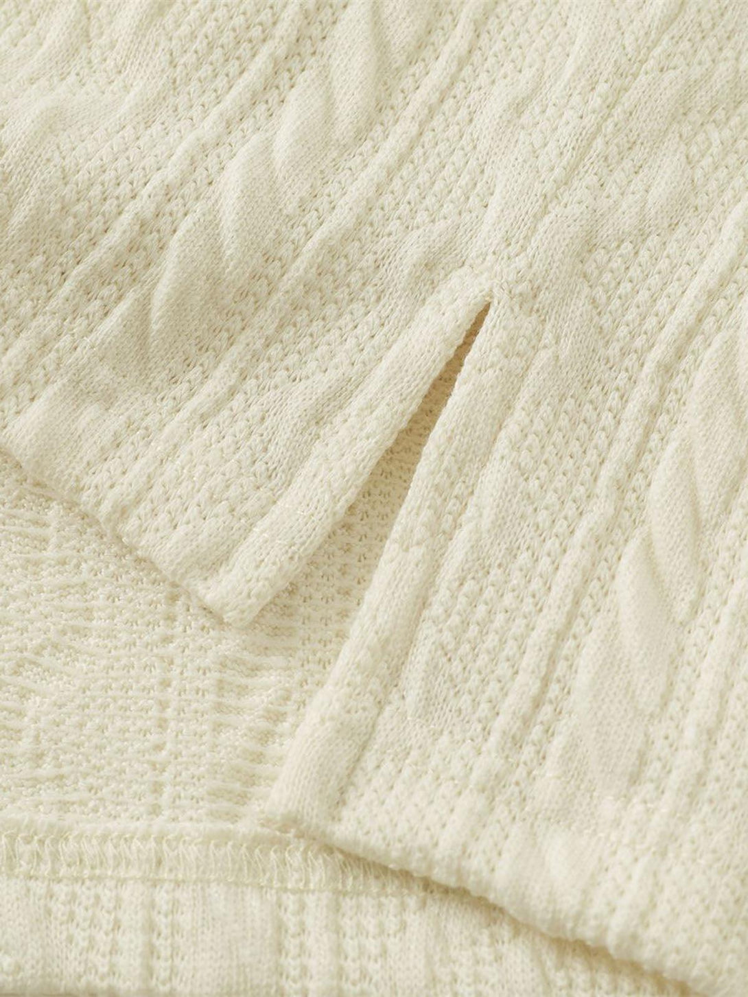 Intricate cable knit texture on a cream sweater by TALISHKO, highlighting cozy details.