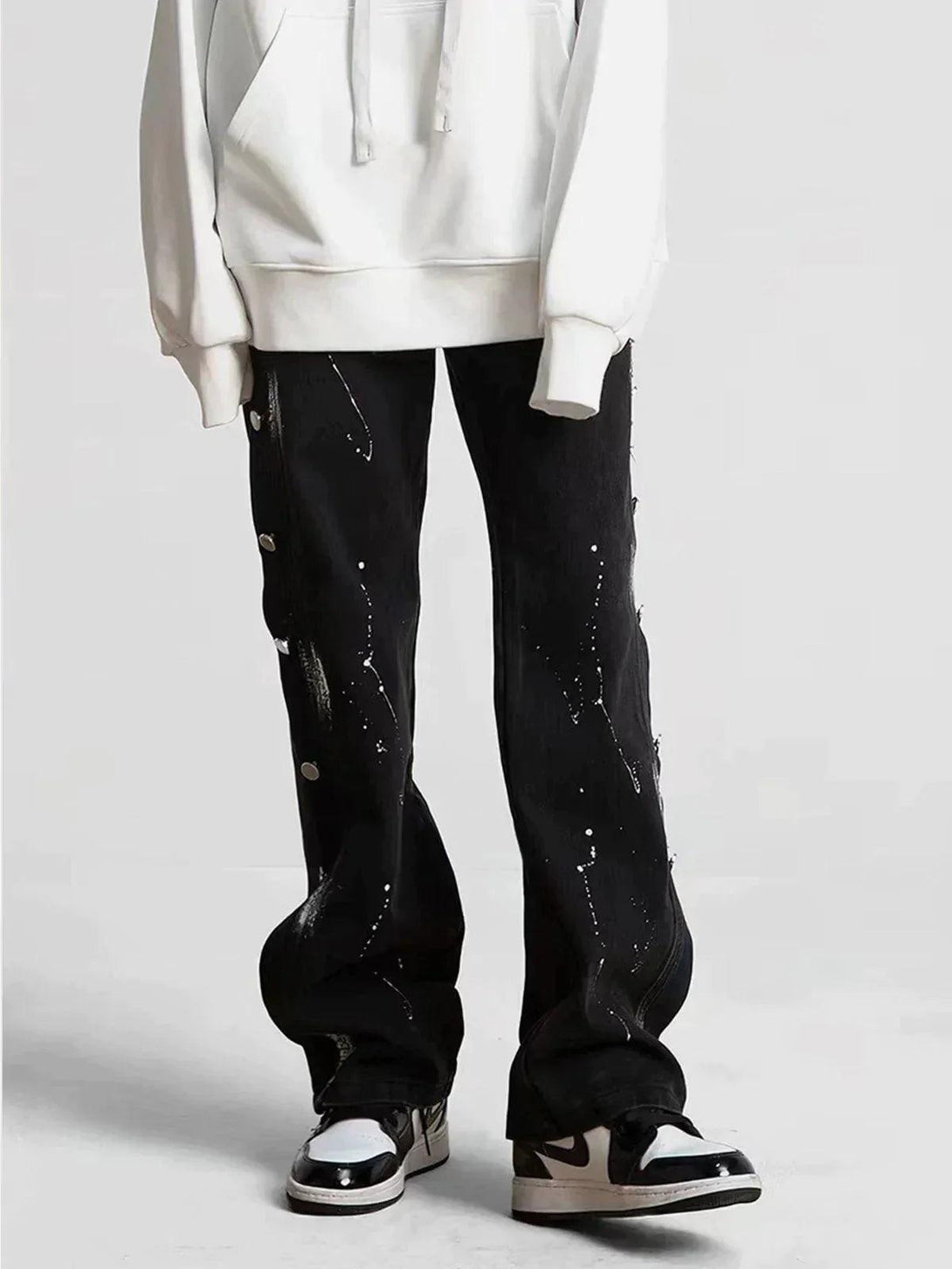 Model wearing black splash ink jeans by TALISHKO, paired with a white hoodie and sneakers.