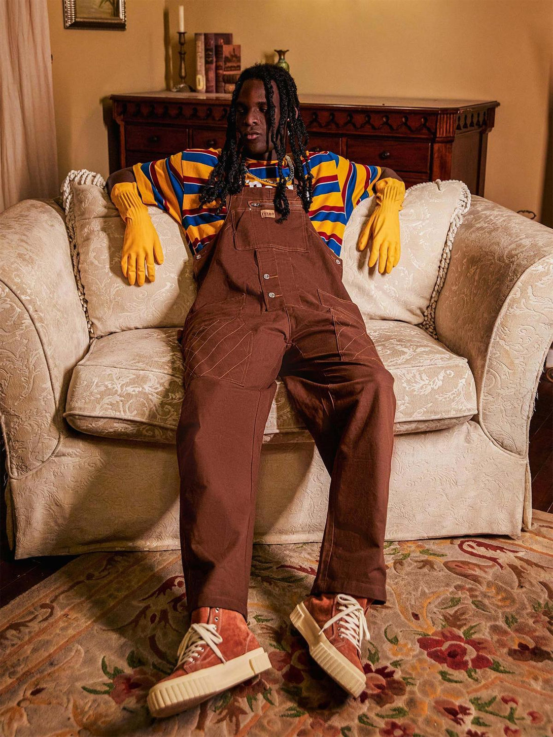 Model wearing TALISHKO vintage straight men's overalls with striped shirt and sneakers on a sofa.