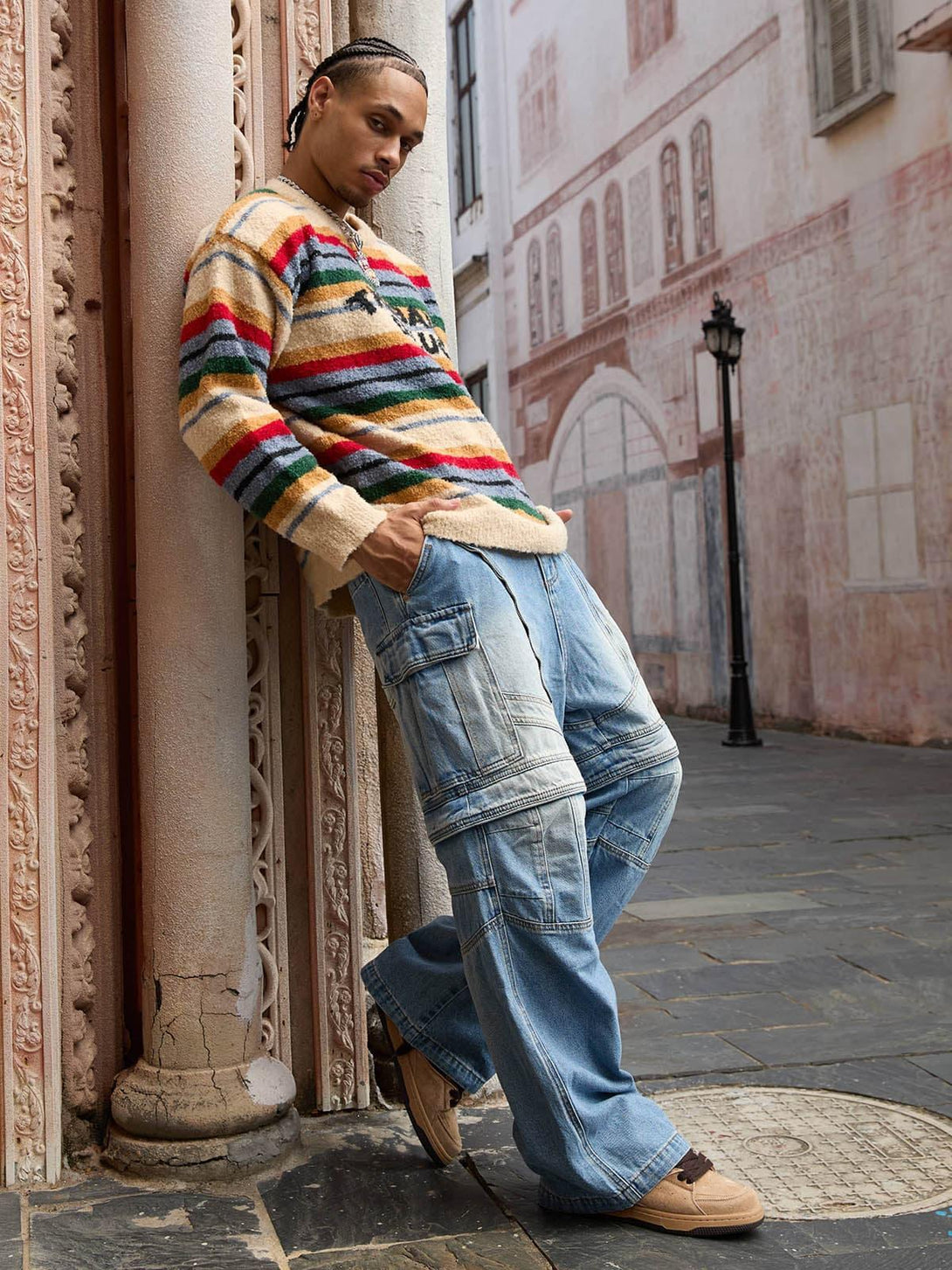 Model leans against ornate columns in a TALISHKO vintage striped sweater and denim pants.