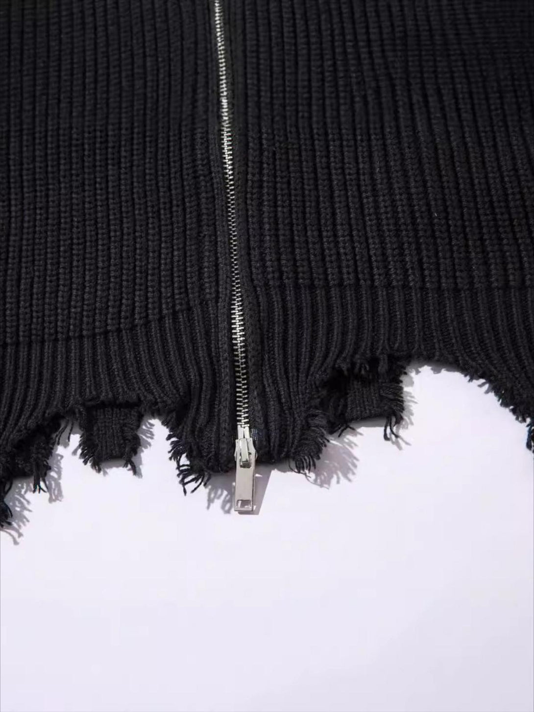 A detailed view of the black ribbed sweater's distressed hem and zipper, crafted by TALISHKO.