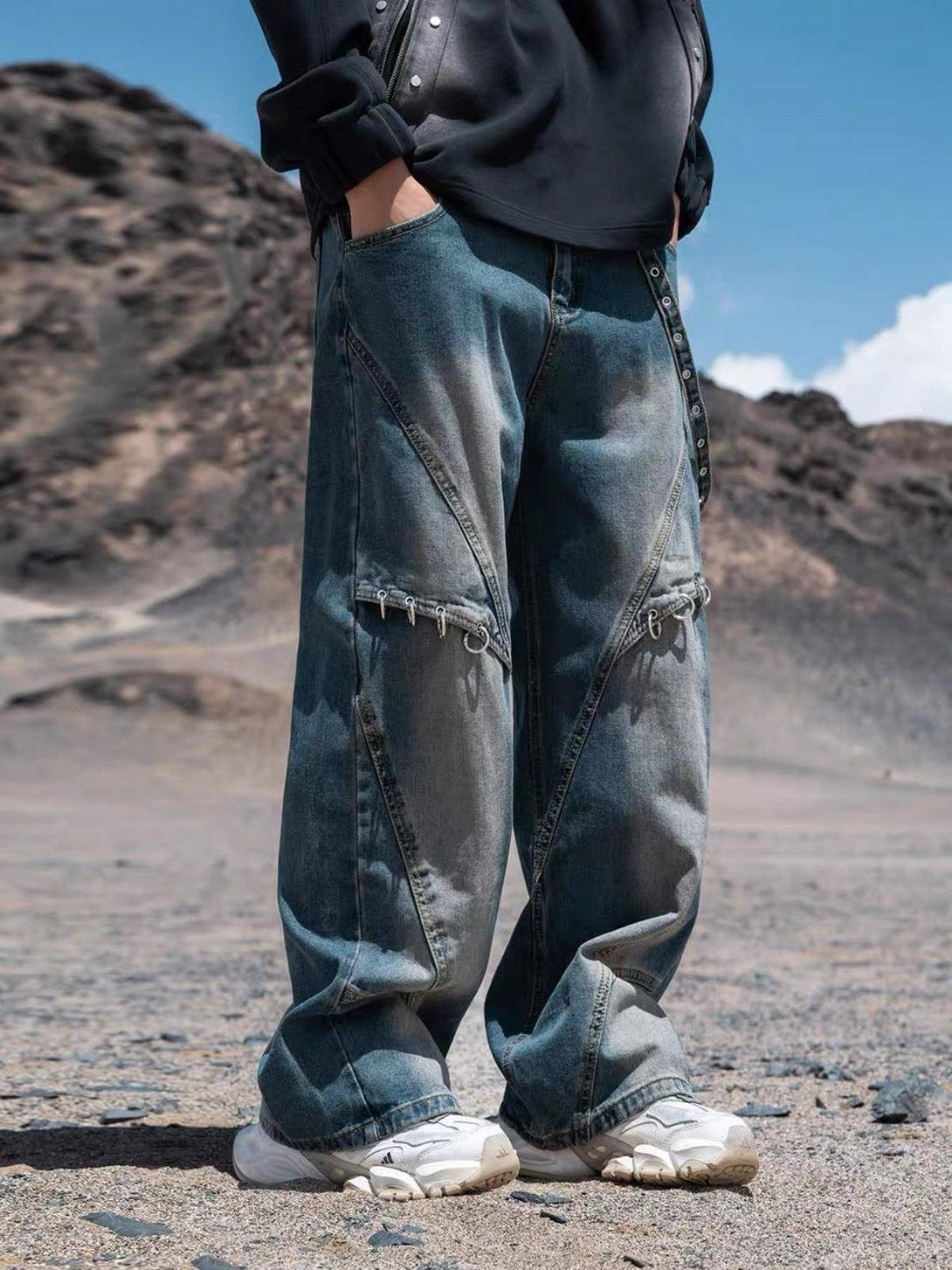 Model wearing TALISHKO washed distressed baggy jeans with unique stitching, set against a rugged landscape.