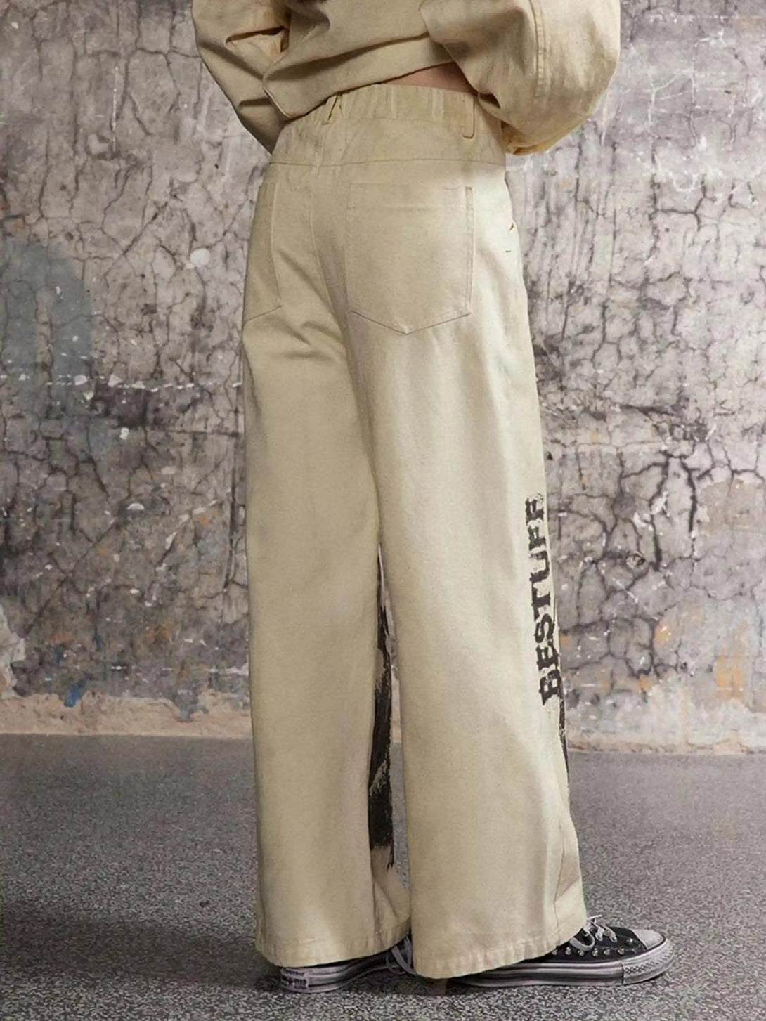 Back view of TALISHKO distressed khaki sweatpants with graffiti detail, styled with sneakers.