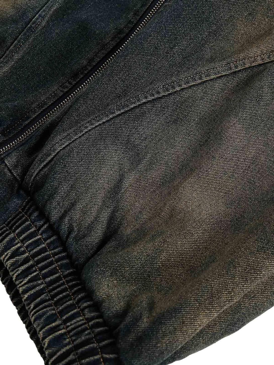 Detailed fabric and stitching of a TALISHKO washed distressed denim jacket, featuring elastic cuffs.