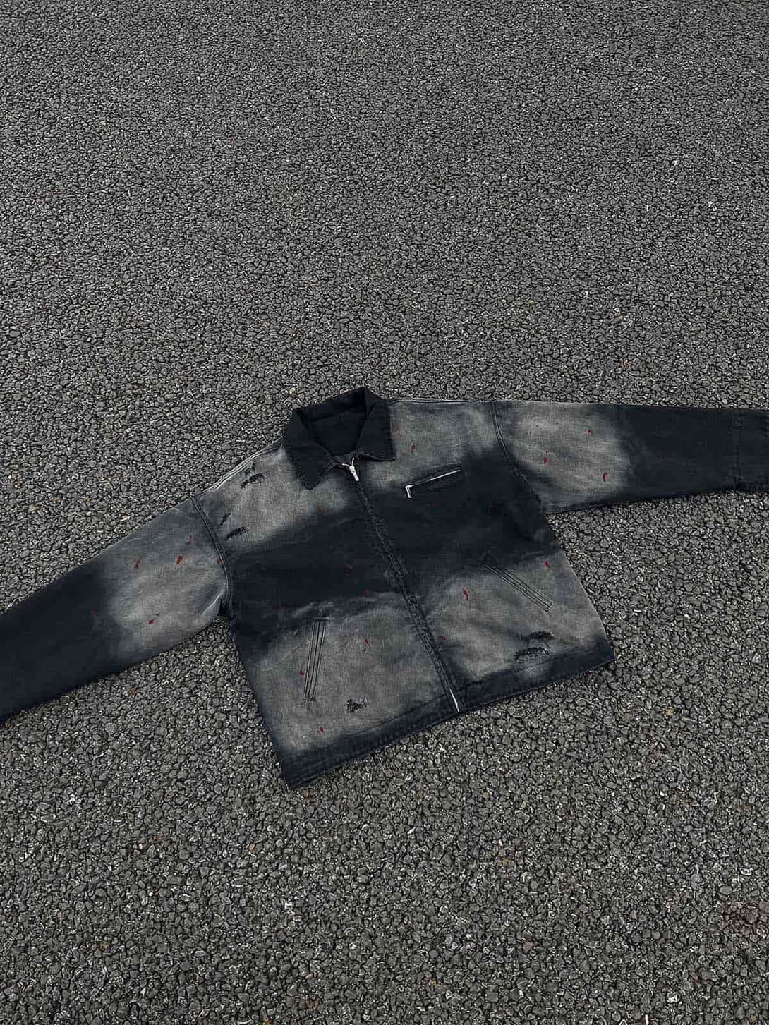 A washed ink gradient denim jacket by TALISHKO, highlighting its unique ripped details on asphalt.