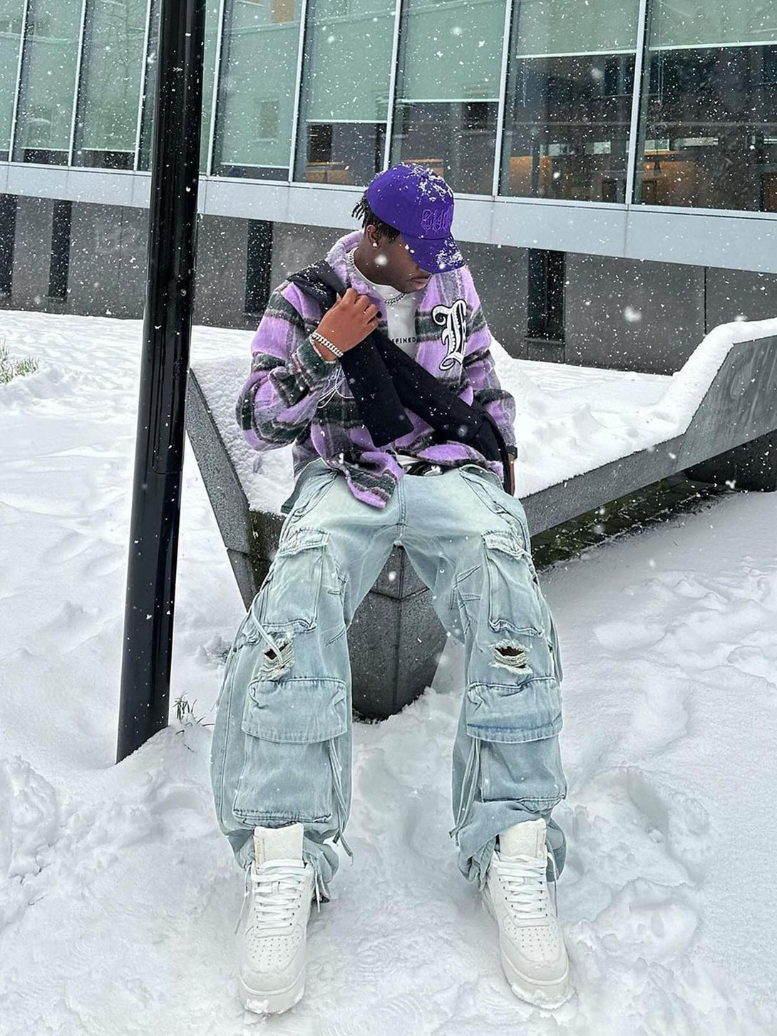 Model in snowy setting wearing TALISHKO washed cargo jeans with multiple pockets and white sneakers.
