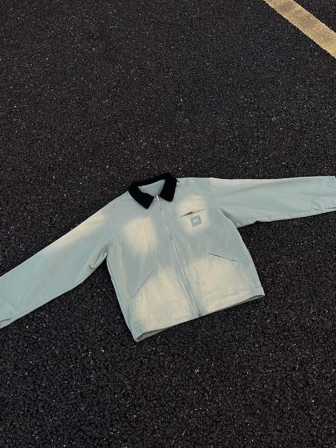 TALISHKO's washed gradient zip-up jacket with black collar on asphalt, emphasizing urban style.