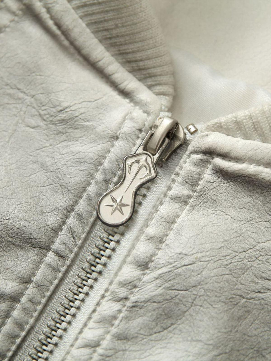 TALISHKO's bomber jacket zip detail with star emblem, highlighting rugged leather texture.