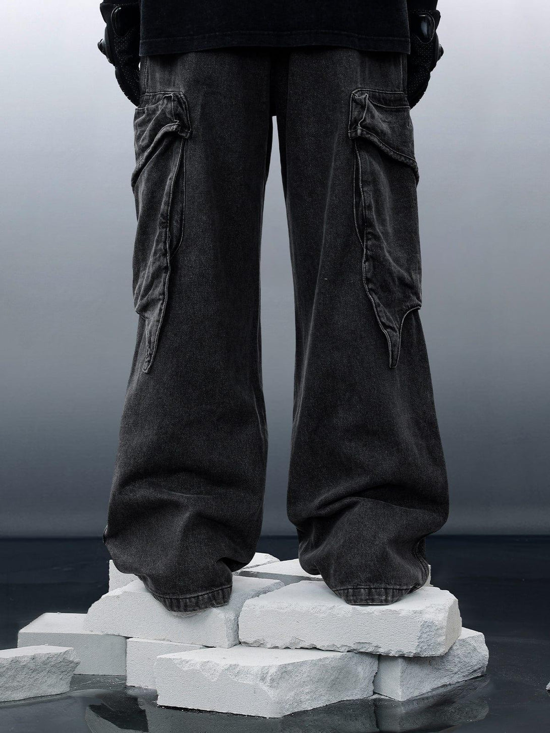 Wide-leg jeans with washed texture and unique pockets, showcased by TALISHKO on a concrete backdrop.