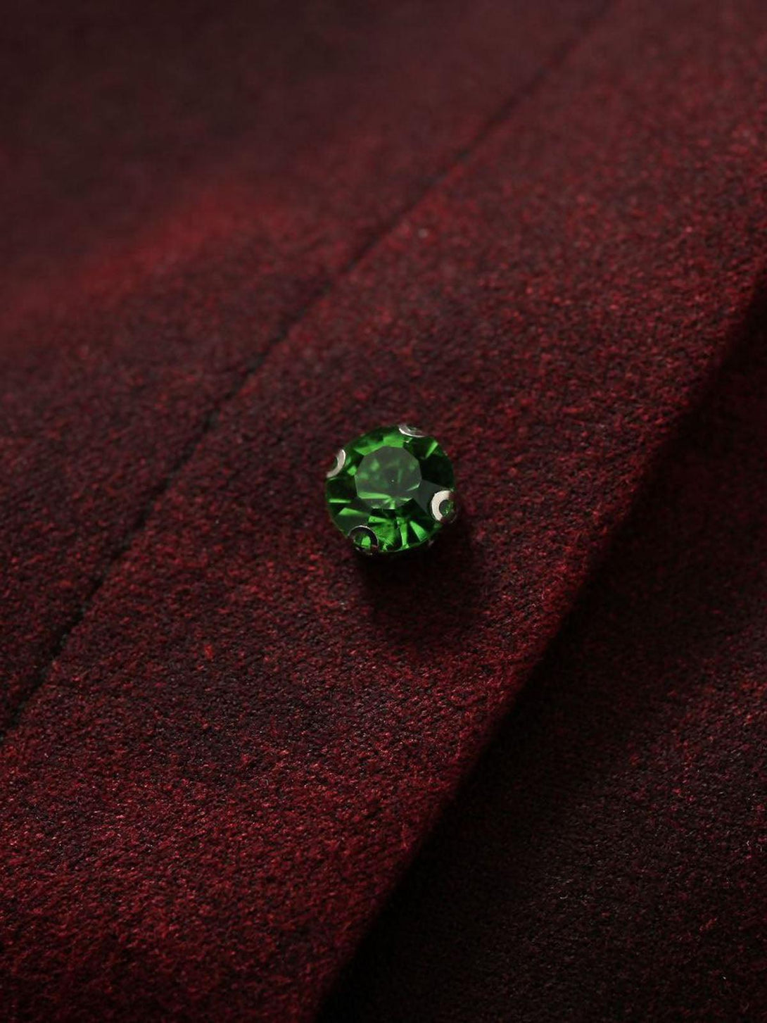 A detailed view of the TALISHKO jacket's green gemstone button against a rich, red fabric.